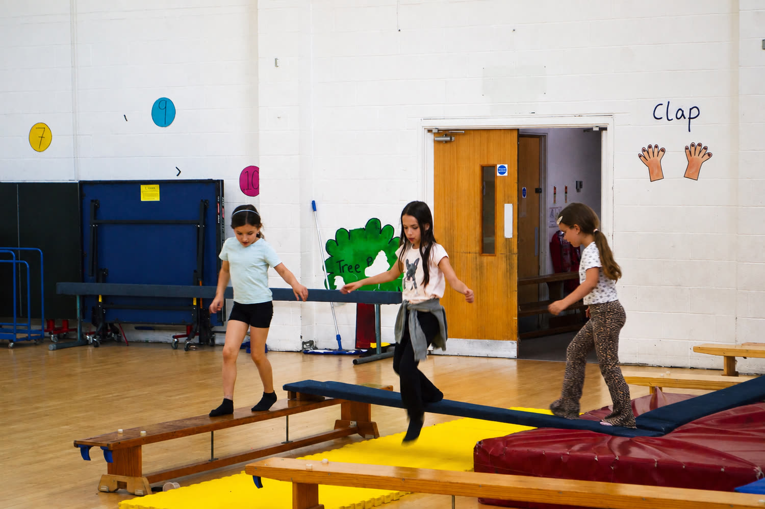 Three children balancing along benches and beams in the school hall