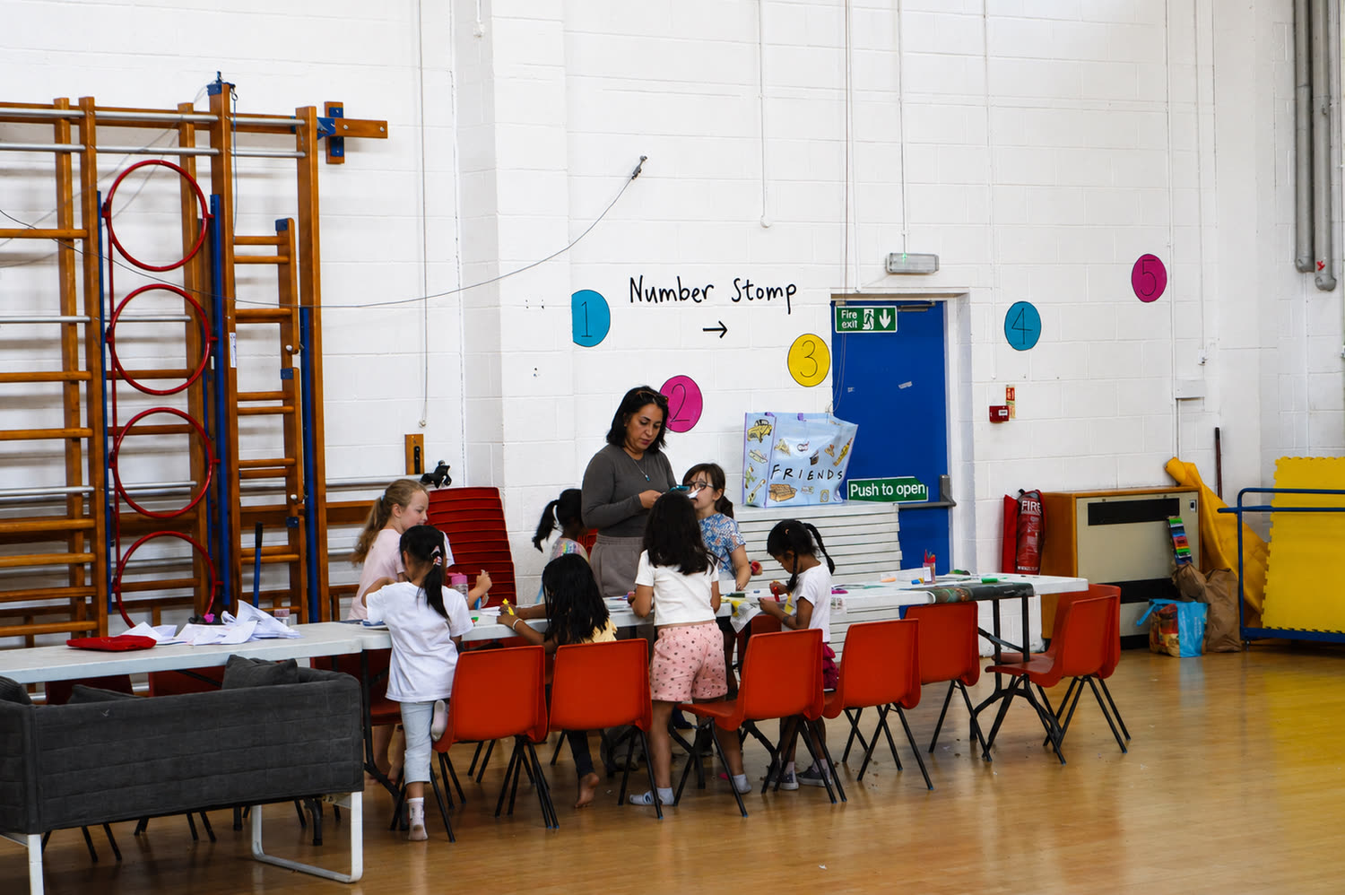 A coach helping children at the craft table in the school hall